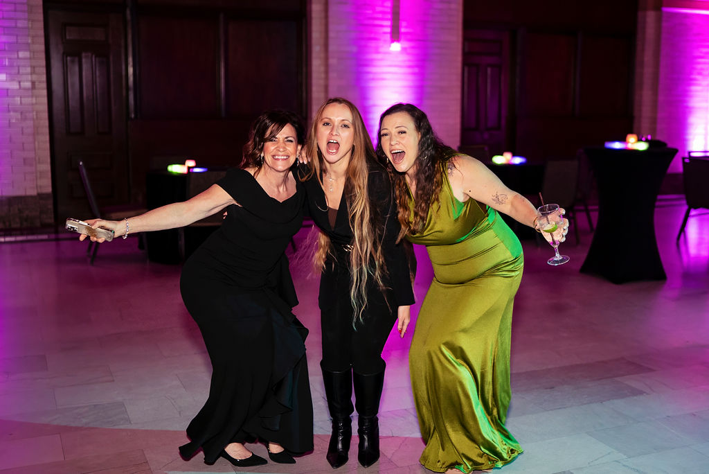 Three women celebrating together on the dance floor at the Women of Work Gala